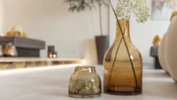 Zwei braune Glasvasen mit weißen Blumen auf einem Tisch in einem Wohnzimmer