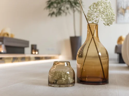 Zwei braune Glasvasen mit weißen Blumen auf einem Tisch in einem Wohnzimmer