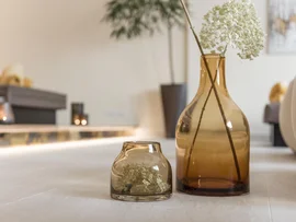 Zwei braune Glasvasen mit weißen Blumen auf einem Tisch in einem Wohnzimmer
