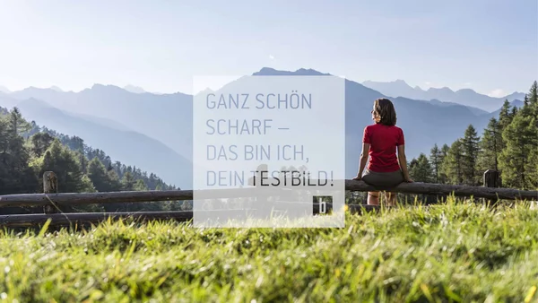 Frau sitzt auf Holzgeländer mit Bergsicht bei sonnigem Wetter