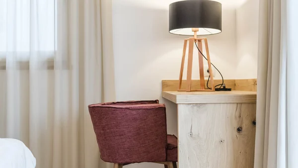 Rotes Stuhl vor Holztisch mit schwarzer Lampenschirmlampe in einem hellen Raum