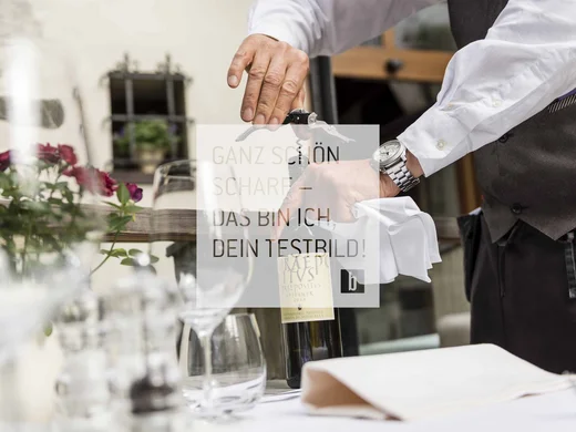 General Kellner öffnet Weinflasche mit Korkenzieher am gedeckten Tisch