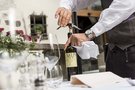 Kellner öffnet Weinflasche mit Korkenzieher am gedeckten Tisch