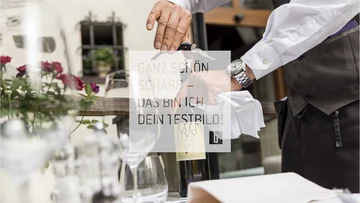 General Kellner öffnet Weinflasche mit Korkenzieher am gedeckten Tisch