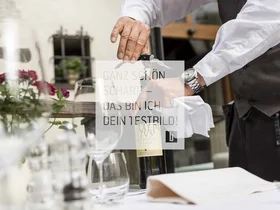 Kellner öffnet Weinflasche mit Korkenzieher am gedeckten Tisch