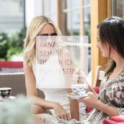 Zwei Frauen trinken Kaffee draußen in einem Café und unterhalten sich