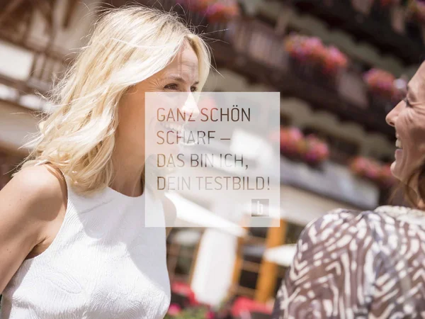 Zwei Frauen lachen und unterhalten sich im Freien vor einem Blumenhaus