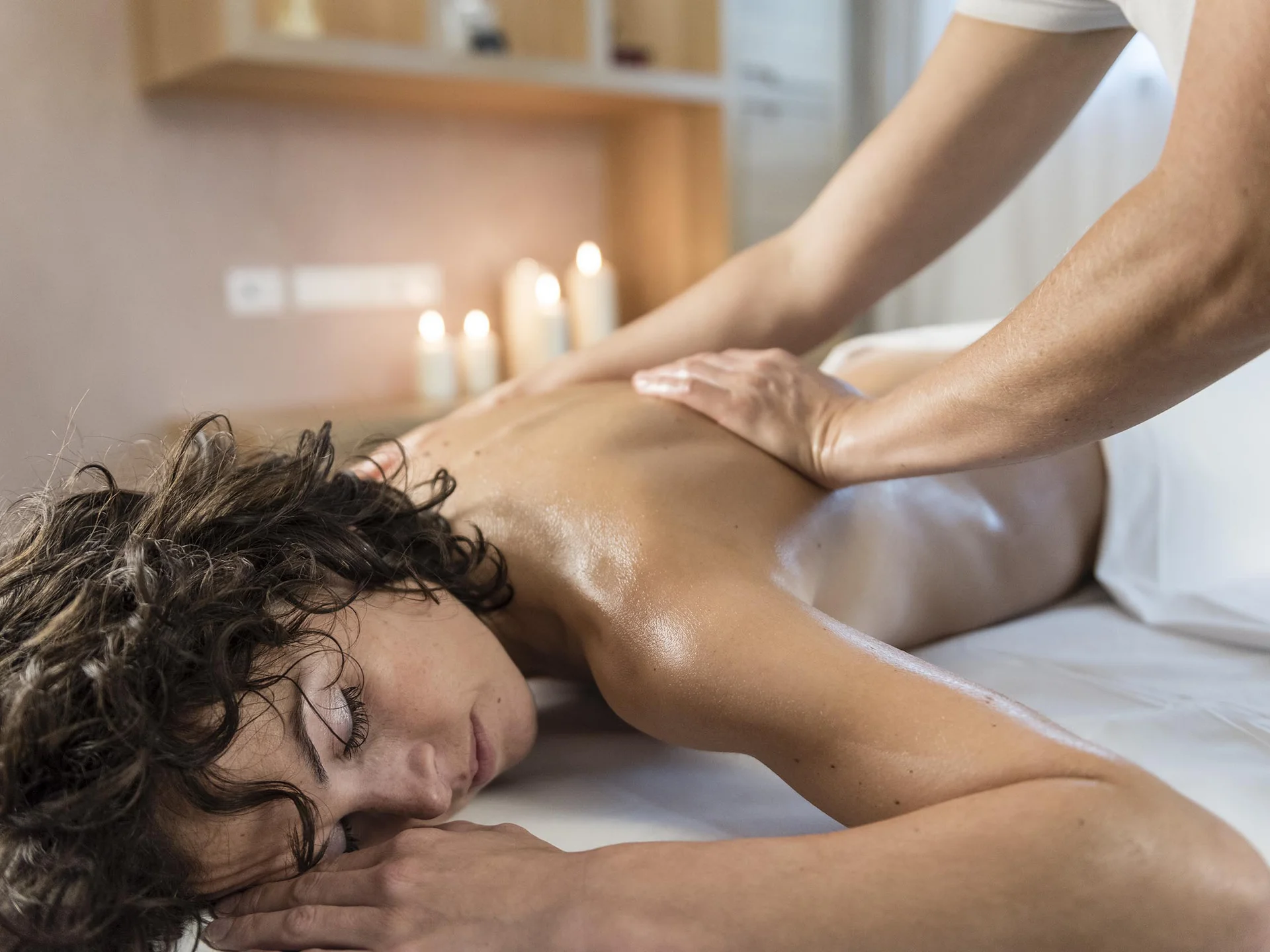 Wellness Frau liegt entspannt bei Massage im Spa mit Kerzen im Hintergrund