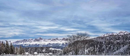 Schneebedeckte Landschaft mit Bergen, Bäumen und blauem Himmel