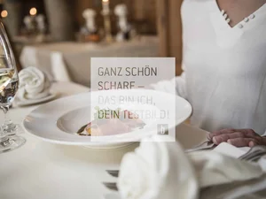 Person sitzt am gedeckten Tisch mit Teller und Weinglas im Restaurant