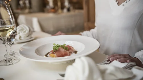 Person sitzt am gedeckten Tisch mit Teller und Weinglas im Restaurant