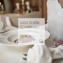 Person sitzt am gedeckten Tisch mit Teller und Weinglas im Restaurant