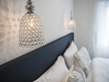 Moderne Kristallwandleuchte über einem gemütlichen Schlafzimmer mit Kissen