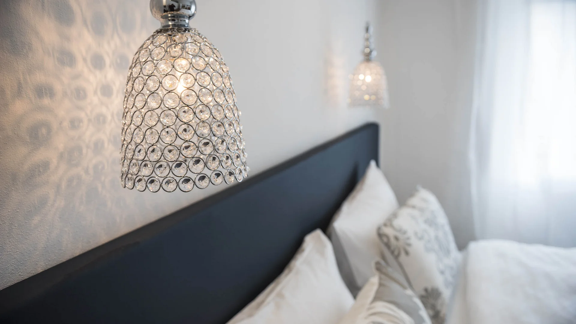 Moderne Kristallwandleuchte über einem gemütlichen Schlafzimmer mit Kissen