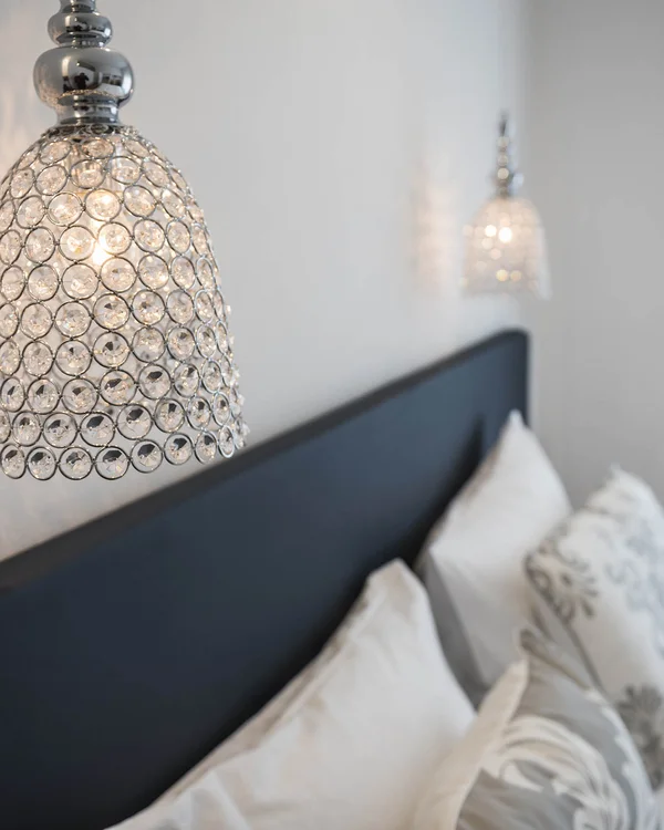 Moderne Kristallwandleuchte über einem gemütlichen Schlafzimmer mit Kissen