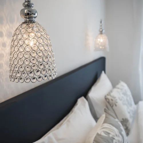 Moderne Kristallwandleuchte über einem gemütlichen Schlafzimmer mit Kissen